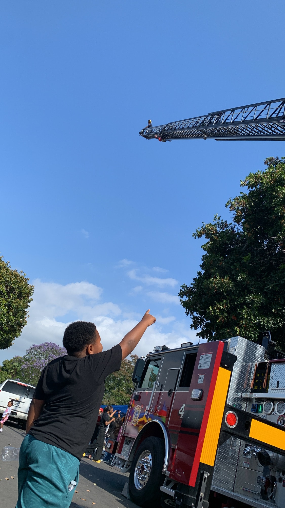 Child pointing up at a fire truck ladder at the Compton field day